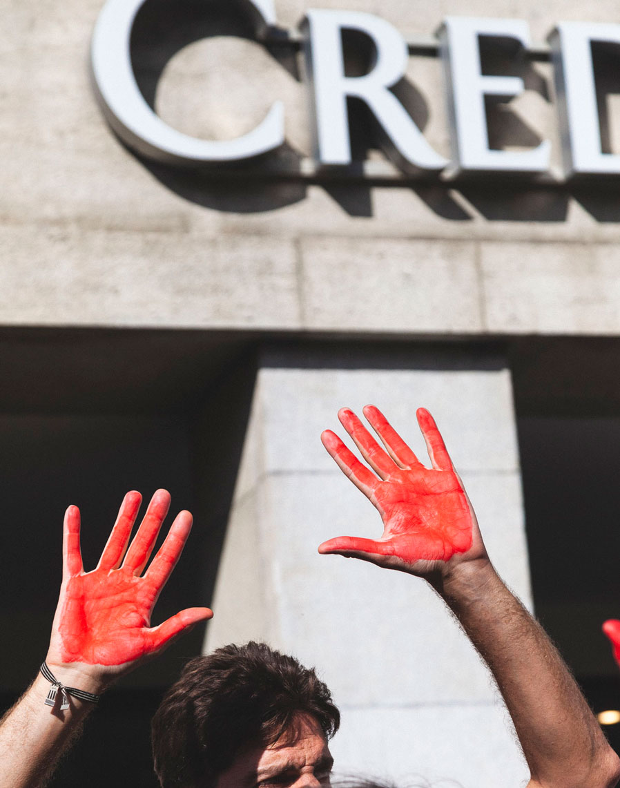 Un manifestant avec les mains peintes en rouge devant le Credit Suisse
