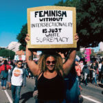 Une manifestante féministe tient une banderole "Feminism without intersectionality is just white supremacy"