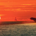 Porte avion USS Ronald Reagan devant un soleil couchant