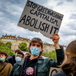 Un manifestant tient une banderole "Stop Greenwashing capitalism, abolish it”