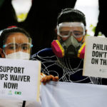 Deux militant-e-s philippins tiennent des pancartes pour la levée des brevets sur les vaccins Covid