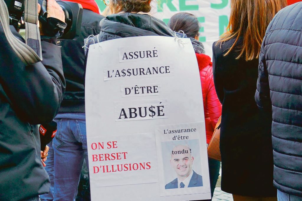 Une manifestante porte un carton avc le portrait d'Alain Berset