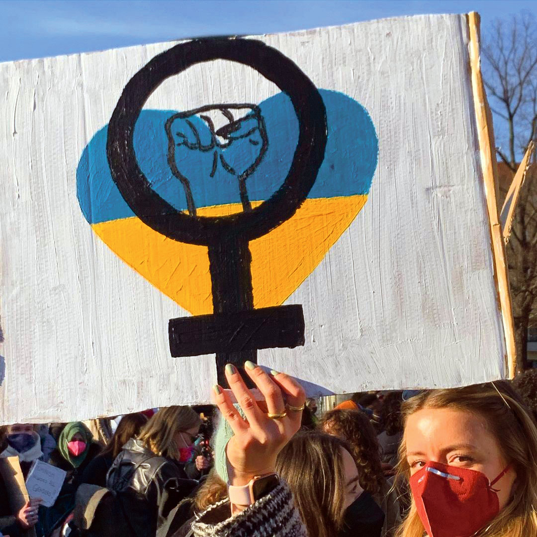 Une manifestante tient une pancarte avec un cœur aux couleurs de l'Ukraine et les symbole féministe