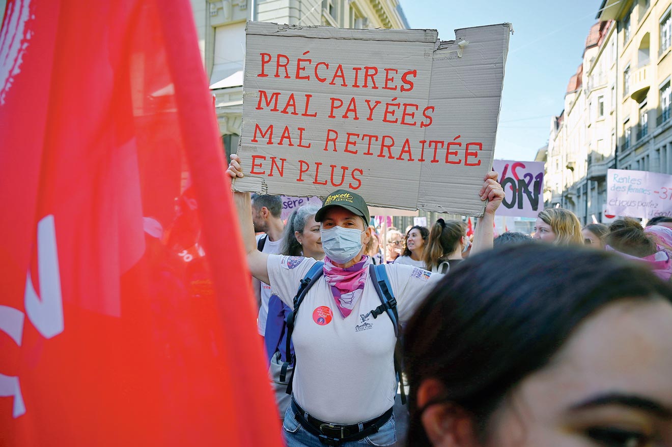 Une manifestante tient une pancarte "précaires, mal payées, mal retraitée en plus”