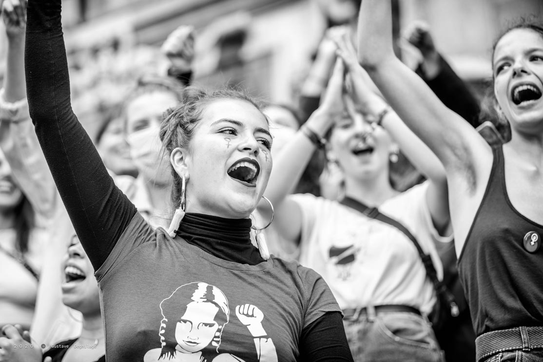 Une femme avec un t-shirt sur lequel une femme lève le poing et un dessin du symbole féministe sur les joues lève le poing