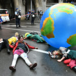 Des manifestants pour le climat couchés sur la route à côté d’une planète gonflable